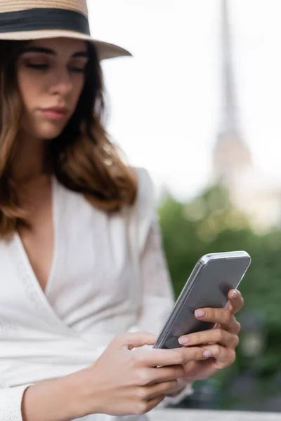 Jovem desfocada de chapéu de sol usando smartphone ao ar livre em Paris — Fotografia de Stock