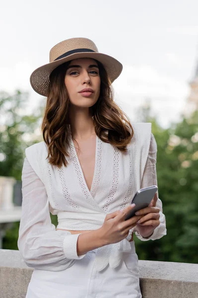 Portrait de femme à la mode tenant un smartphone et regardant la caméra dans la rue à Paris — Photo de stock