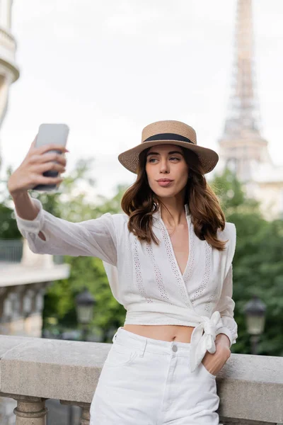 Trendy woman taking selfie on blurred cellphone with Eiffel tower at background in Paris — Stock Photo