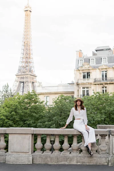 Fashionable woman holding smartphone and looking at camera on street with Eiffel tower at background in Paris — Stock Photo
