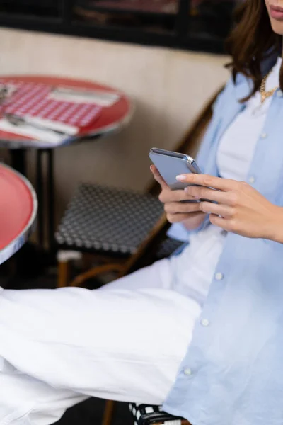 Vue recadrée d'une femme élégante utilisant un smartphone sur la terrasse d'un café à Paris — Photo de stock