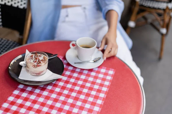 Cropped view of tiramisu and coffee near blurred woman on cafe terrace in France — Stock Photo
