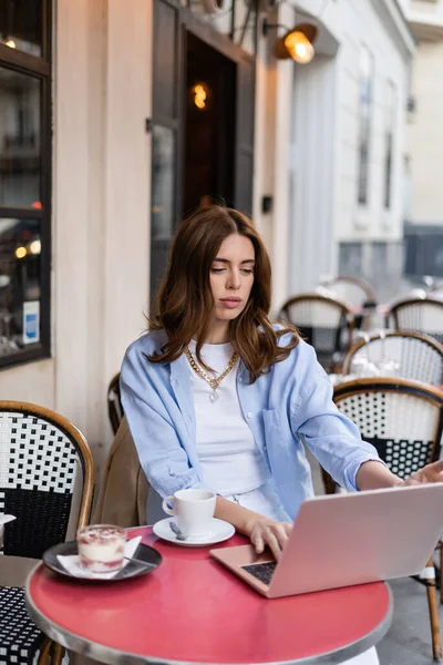 Freelance tendance utilisant un ordinateur portable près du café et du dessert dans un café en plein air à Paris — Photo de stock