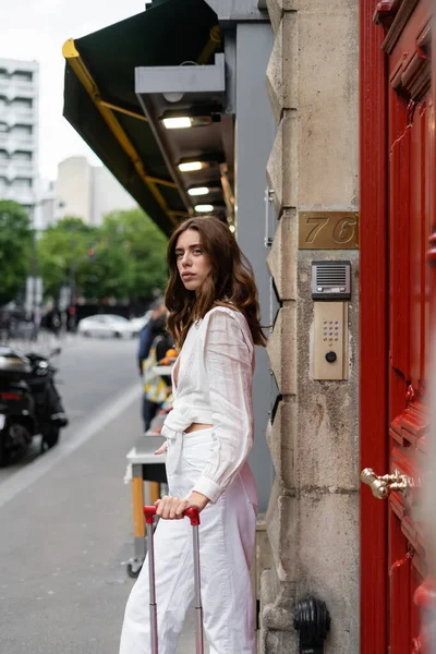 Stylish woman standing near suitcase and building on urban street in France — Stock Photo