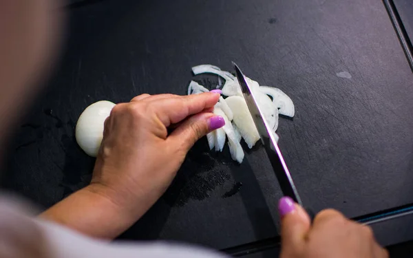 Kadın siyah tahtada soğan kesiyor, yemek hazırlıyor.