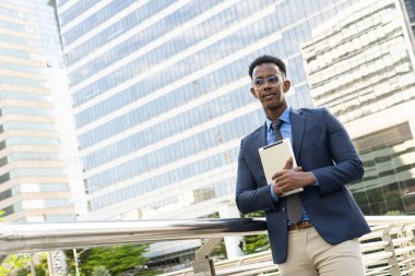 Şehirdeki iş adamları. Yakışıklı bir iş adamının portresi. Modern iş adamı. Kendine güvenen, takım elbiseli ve gözlüklü genç bir adam arka planda şehir manzarasıyla dışarıda dikilirken.