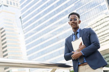 Şehirdeki iş adamları. Yakışıklı bir iş adamının portresi. Modern iş adamı. Kendine güvenen, takım elbiseli ve gözlüklü genç bir adam arka planda şehir manzarasıyla dışarıda dikilirken.