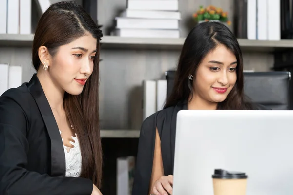 Two women with laptop in open space office. Business concept. Young women in office working together on desktop.