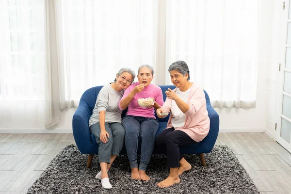 Group of happy elderly women sitting on sofa ready to watch TV. Group of asian old senior female spending weekend time together.