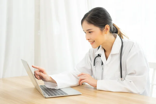 Asian female doctor using laptop computer online video call remote talking to patient. Medical practitioner giving online virtual consultation to patient from hospital office.