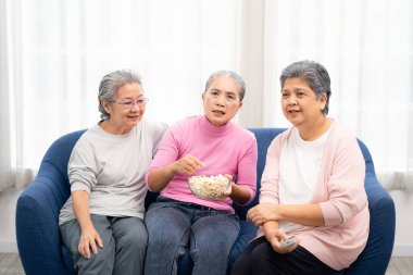 Bir grup mutlu yaşlı kadın kanepede oturup televizyon seyretmeye hazır. Asyalı yaşlı bir kadın grubu hafta sonunu birlikte geçiriyorlar.. 