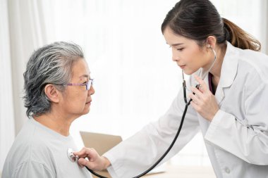 Asya 'lı yaşlı bir kadını kontrol etmek için steteskop kullanan kadın doktor ve tedavi, sağlık sigortası, yaş, destek, sağlık hizmetleri ve insanların konsepti hakkında konuşuyor 