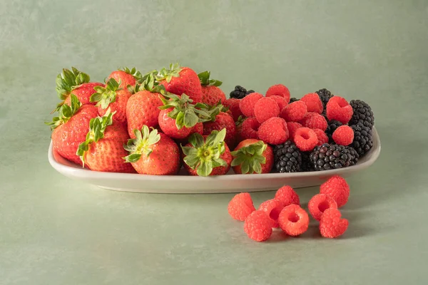 Porcelain platter with strawberries, raspberries and blackberries isolated on a greenish background