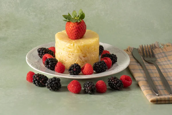Böğürtlen ve ahududu dolu porselen bir tabakta doğal ananas dilimleri.