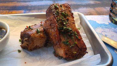 Tabağa otlar serpiştirilmiş iki parça lezzetli pirzola. Yakınlarda çok lezzetli soslu küçük bir tabak var.