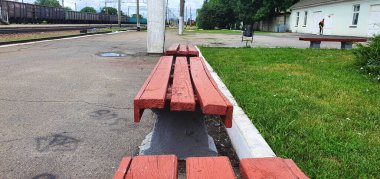Empty benches at a railway station in central Ukraine. Old wooden benches painted with red paint. Wood cracked and warped