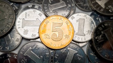 Sarı bir Çin 5 jiao sikkesinin yakın plan çekimi. Arka planda bir sürü Çin Yuan parası var. 2014 'te 5 jiao sikkesi basıldı.