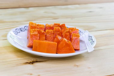 Olgun papaya, ahşap bir masada tabakta parçalara ayrılır. Olgun meyve, tatlı, lezzetli ve yüksek besin değeri vardır.