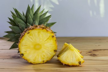 Tahta bir masanın üzerinde yarım ve dilimlenmiş ananas, yakın çekim, tatlı ve ekşi meyve, besleyici ve yüksek vitamin