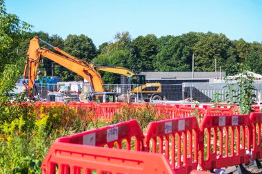 Arka planda yeşil ağaçlar ve mavi gökyüzü olan çakıl taşlı bir inşaat alanında sarı yol vinci.