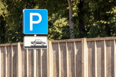 Arkasında yeşil ağaçlar ve beton çitler olan araba park yeri tabelası.