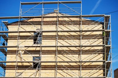 Metal askılı kahverengi tuğla bir ev ve yanında da koyu yeşil bir ağaç.