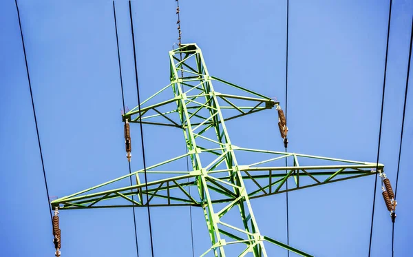 Green electricity pole with black wires and blue sky background
