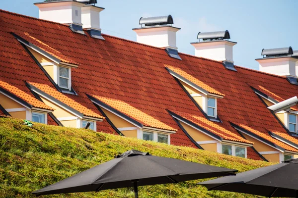 A white house with many windows and brown roof tiles with green grass and black umbrellas