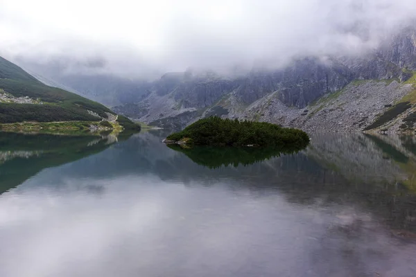 Mountain in the Polish Tatras with a small turquoise lake and rocks in the middle of the mountain with white fog and clouds