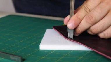 Adam deriyi yumruklarla delip iplik dikmek için delik açıyor. Bir adam deride delikler açıyor. orta plan çerçevesi.