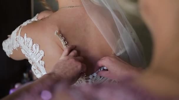 妈妈帮助新娘穿上衣服 手把白色的钮扣固定在背面 穿婚纱的过程 婚礼的沉闷 新娘和她妈妈穿上婚纱 — 图库视频影像