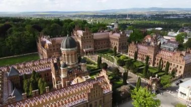 Kuleleri ve kubbeleri olan eski bir tarihi üniversite binası. Binanın etrafında bahçeler, yeşillikler var. Chernivtsi Ulusal Üniversitesi.