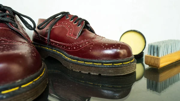 This maroon wingtip brogue made of genuine leather was photographed with a brush and shoe polish on a white background