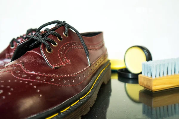 This maroon wingtip brogue made of genuine leather was photographed with a brush and shoe polish on a white background