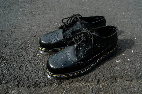 Detail view of men\'s classic black genuine leather brogue wingtip shoes with rubber soles, photographed outdoors during the day
