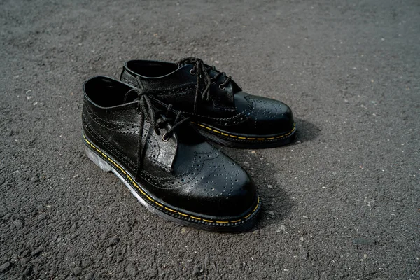 Detail view of men's classic black genuine leather brogue wingtip shoes with rubber soles, photographed outdoors during the day