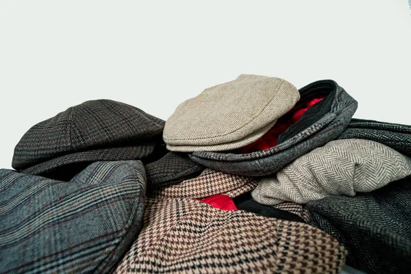 Pile of newsboy caps and flat caps in various colors and designs on a white background