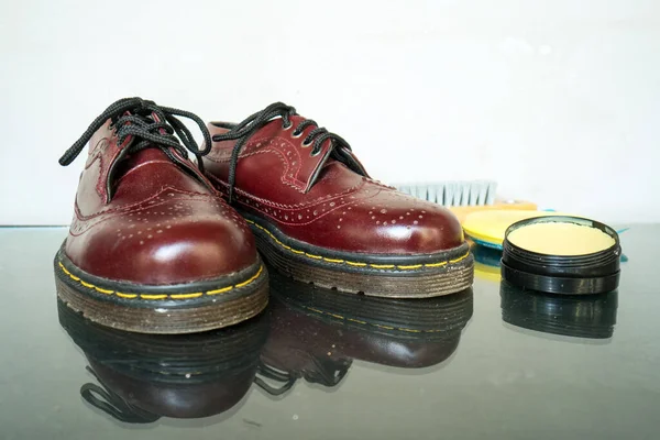 This maroon wingtip brogue made of genuine leather was photographed with a brush and shoe polish on a white background