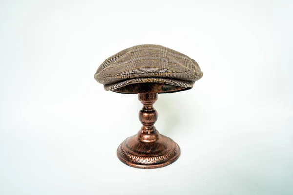 Detail of scally cap or flat cap in dark brown pattern  herringbone tweed fabric set on a bronze head mannequin on a white background