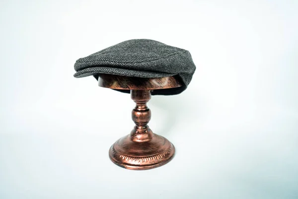 Detail of scally or flat cap in midnight-dark-black herringbone tweed fabric set on a bronze head mannequin on a white background