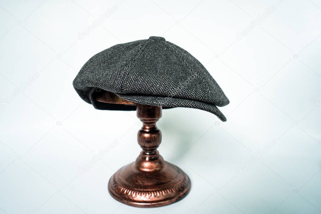 Detail of a classic eight-panel newsboy hat in black base, in herringbone wool fabric set on a bronze head mannequin on a white background