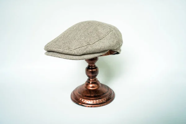 Detail of scally or flat cap in dark brown pattern  herringbone tweed fabric set on a bronze head mannequin on a white background