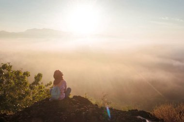 Silhouettes of local tourists enjoying the beautiful romantic sunrise with views of hills, white mist and golden yellow sky at Black Hill, Yogyakarta, Indonesia