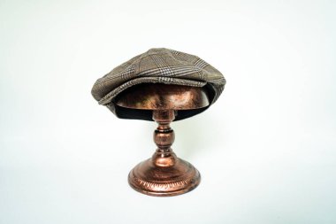 Detail of a classic eight-panel newsboy hat, in dark brown herringbone tweed fabric set against a bronze head mannequin on a white background