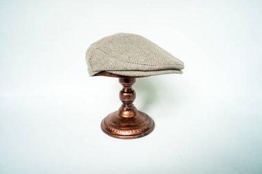 Detail of scally or flat cap in dark brown pattern  herringbone tweed fabric set on a bronze head mannequin on a white background