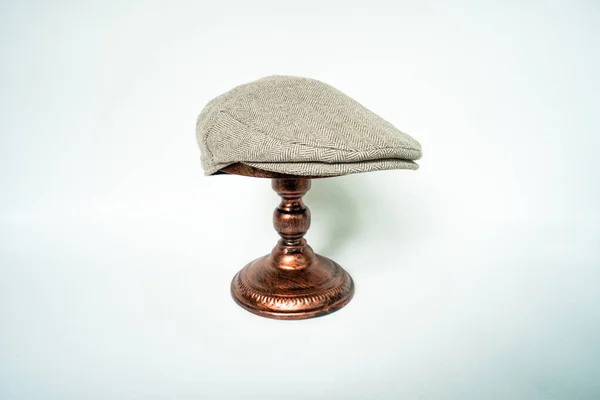 Detail of scally or flat cap in dark brown pattern  herringbone tweed fabric set on a bronze head mannequin on a white background