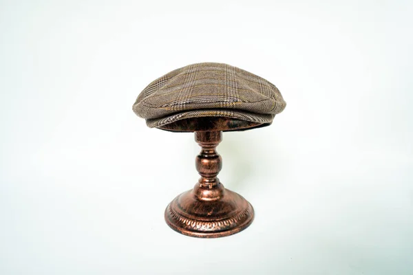 Detail of scally cap or flat cap in dark brown pattern herringbone tweed fabric set on a bronze head mannequin on a white background