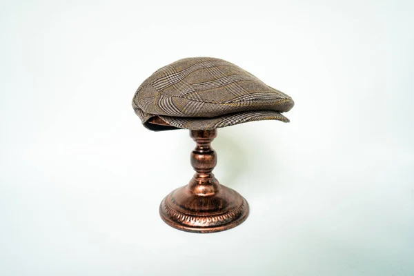 Detail of scally cap or flat cap in dark brown pattern herringbone tweed fabric set on a bronze head mannequin on a white background