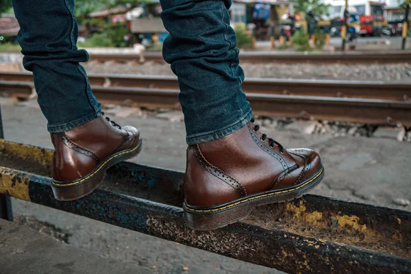 Close up of a dark brown 8-hole wingtip brogue boot when worn for a walk on the railroad track when the evening sky was dark and cloudy