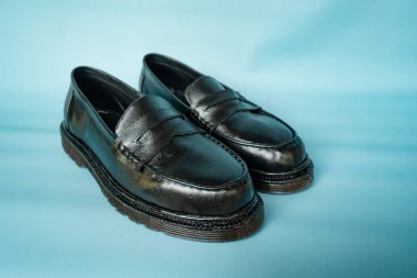 Turkuaz arka planda ayakkabı ustaları tarafından el işçiliğiyle hazırlanmış hakiki sığır derisinden yapılmış tam siyah püsküllü ayakkabıların ayrıntıları.